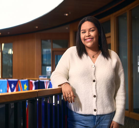 Une femme se tient les bras croisés à côté d’une fenêtre